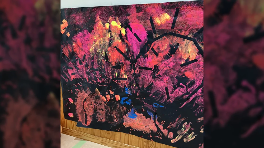 黒い画用紙にピンクとオレンジが弾けるように描かれた、こどもたちのカラフルな作品