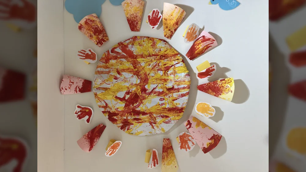 絵の具で取ったこどもたちの小さな手形・足形が丸く並べられ、大きな太陽のように輝く作品